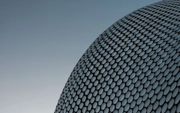 A modern building with a curved façade covered in numerous evenly spaced, silver circular tiles against a clear sky.