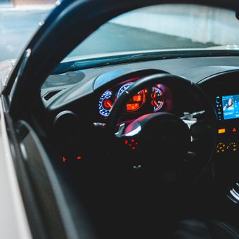 View of a car's interior at night, showing illuminated dashboard, steering wheel, and infotainment screen with a parking lot in the background.