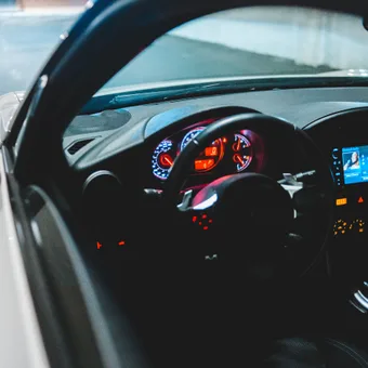 View of a car's interior at night, showing illuminated dashboard, steering wheel, and infotainment screen with a parking lot in the background.