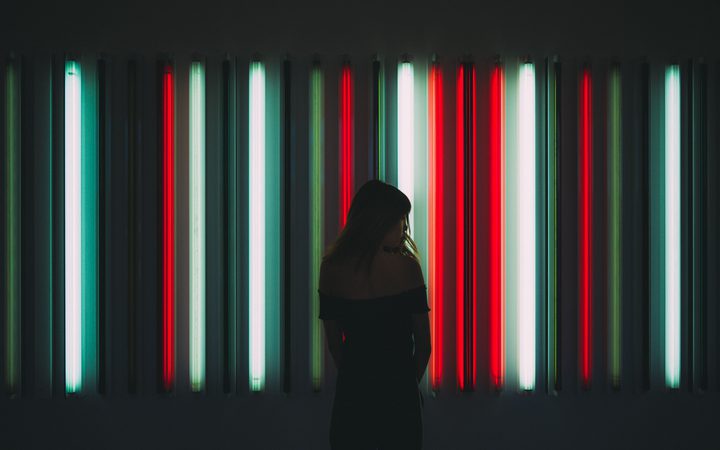 A woman stands in silhouette against a backdrop of colourful vertical neon light tubes in an art installation.