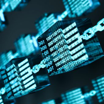 A person with short hair and glasses wearing a dark navy blazer and light blue shirt, smiling softly against a plain gray studio background.