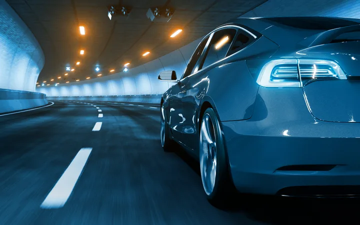 A sleek blue car driving through a lit tunnel, captured from the rear side with motion blur on the road and background lights.