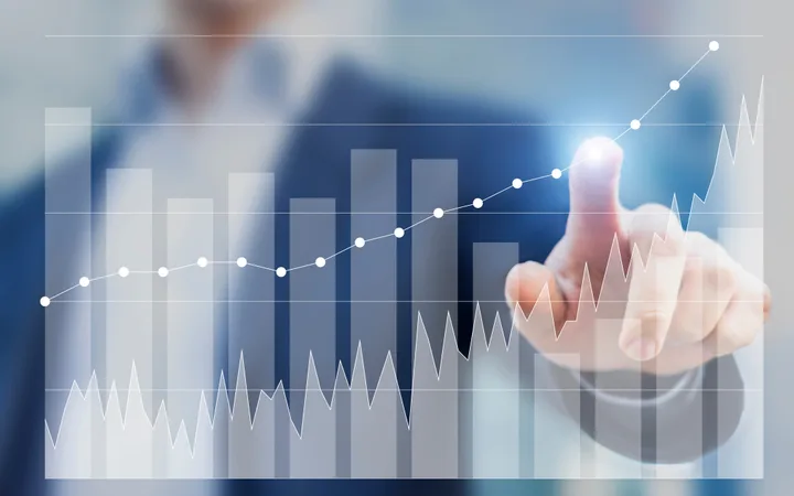 A person in a business suit interacts with a transparent digital graph showing upward trends, bar charts, and line graphs against a blurred background.