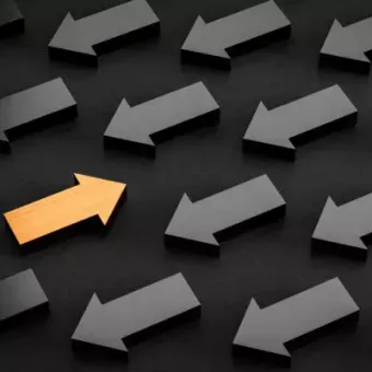 A collection of black arrows pointing left, with one gold arrow pointing right among them on a dark background.