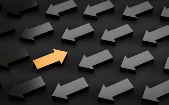 A collection of black arrows pointing left, with one gold arrow pointing right among them on a dark background.