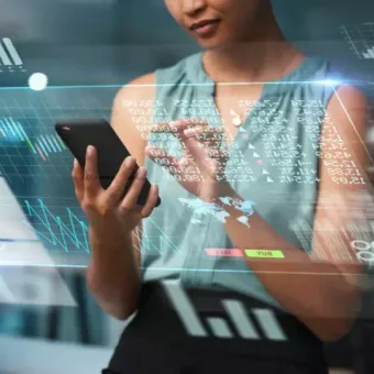 A woman interacts with a smartphone surrounded by digital graphs and data visualisations in a high-tech environment.