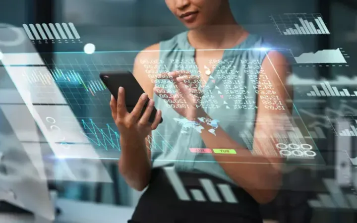 A woman interacts with a smartphone surrounded by digital graphs and data visualisations in a high-tech environment.