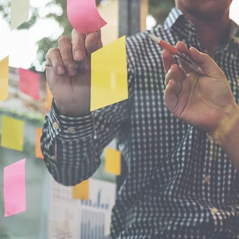 People collaborating and placing colorful sticky notes on a glass wall during a brainstorming session.