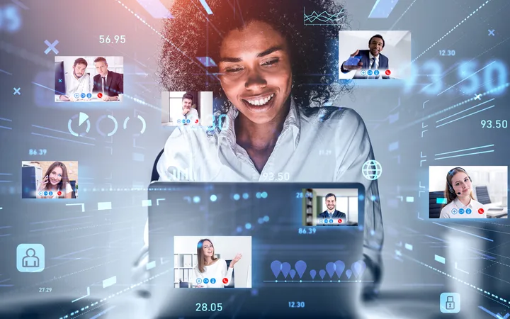 A woman interacts with a virtual video conferencing interface featuring multiple colleagues' images and data visuals in a futuristic digital setting.