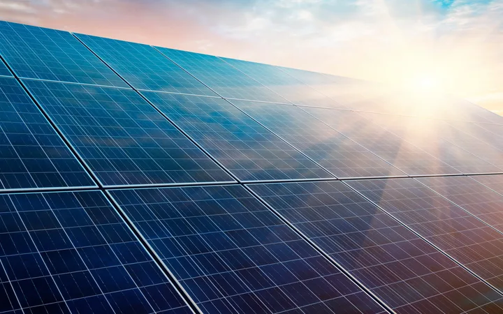 Rows of blue solar panels tilt towards a bright sun, under a warm sunrise sky.