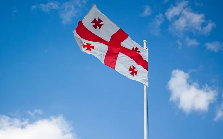 A flag with red crosses on a white background waving against a blue sky with scattered clouds.