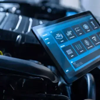 Person holding a tablet displaying vehicle diagnostics over an open car hood with engine components visible.