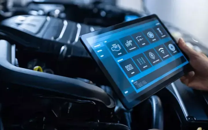 Person holding a tablet with a vehicle diagnostics interface, near the engine of a car.