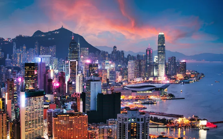 A vibrant city skyline at dusk with illuminated skyscrapers, Mountaintop, and Victoria Harbour in the background.