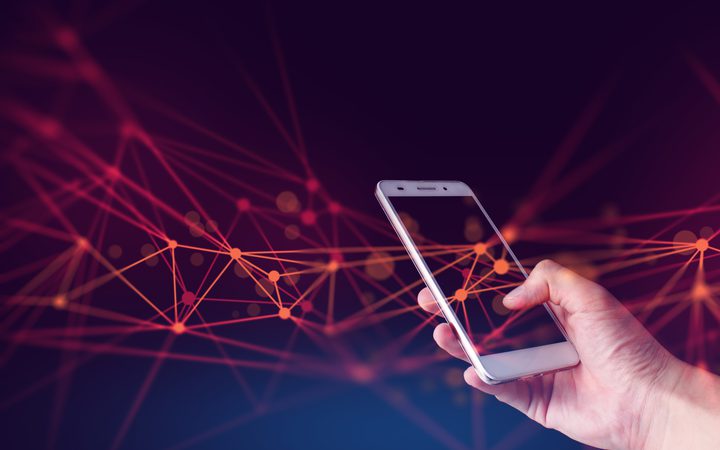 A hand holding a smartphone against a dark background with connected orange and pink network nodes and lines.