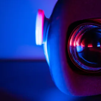 Close-up of a camera lens with vibrant red and blue neon lights, creating a futuristic and dynamic visual effect.