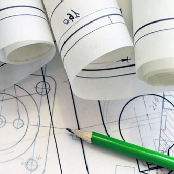 Portrait of a person with long blonde hair, wearing a black blazer over a white polka-dot blouse, smiling against a grey studio backdrop.