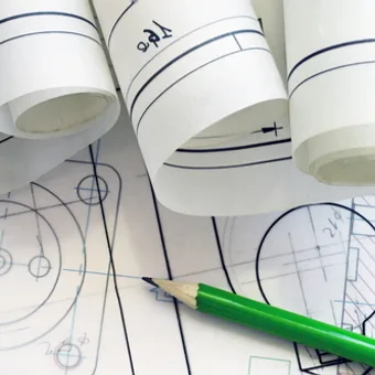 Portrait of a person with long blonde hair, wearing a black blazer over a white polka-dot blouse, smiling against a grey studio backdrop.