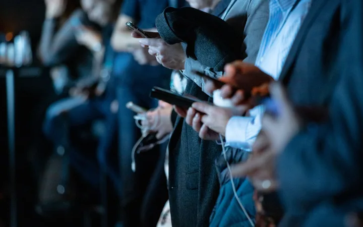 People in formal attire using smartphones and tablets at an indoor event, focusing on their devices with a blurred background.