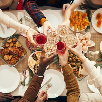 Top-down view of a diverse group toasting with wine glasses around a festive table filled with snacks, pastries and roasted dishes.