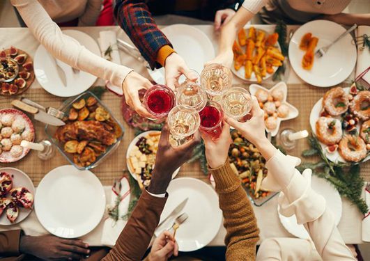 Top-down view of a diverse group toasting with wine glasses around a festive table filled with snacks, pastries and roasted dishes.