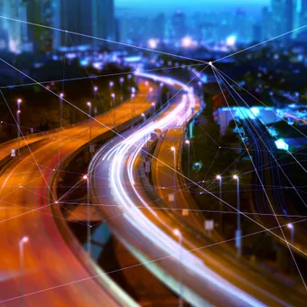 Nighttime highway with light trails, overlaid with a digital network of interconnected lines and nodes across an urban cityscape.