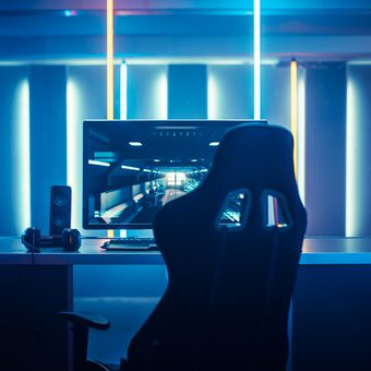 A futuristic gaming or e-sports setup with a computer monitor displaying a virtual environment, surrounded by neon blue and yellow lighting.