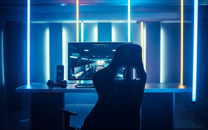 A futuristic gaming or e-sports setup with a computer monitor displaying a virtual environment, surrounded by neon blue and yellow lighting.