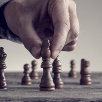 A hand moving a chess piece on a chessboard, with several other pieces visible in the background.