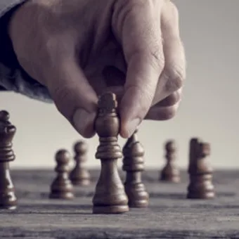 A hand moving a chess piece on a chessboard, with several other pieces visible in the background.