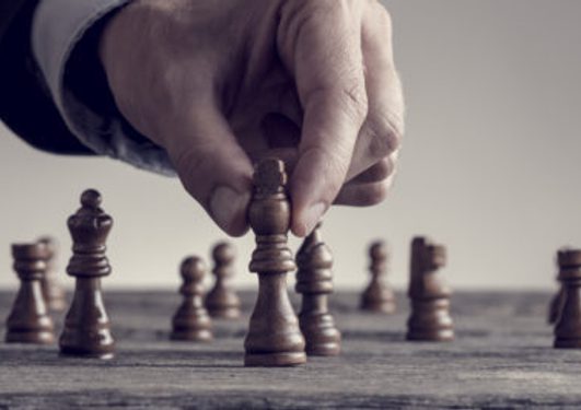 A hand moving a chess piece on a chessboard, with several other pieces visible in the background.