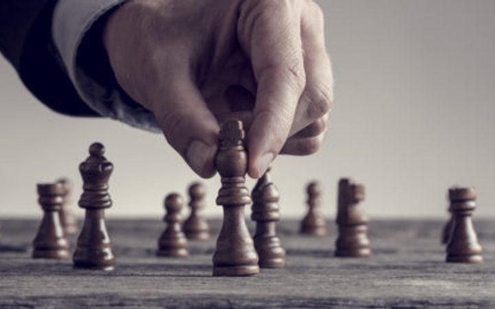 A hand moving a chess piece on a chessboard, with several other pieces visible in the background.