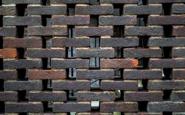Mur en briques rouges et noires avec des espaces entre les briques, vue en gros plan.