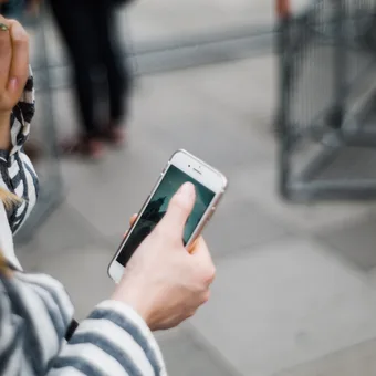 Person holding a smartphone with a photo of a pyramid, standing near a shopping cart in an outdoor area with a tiled pavement.