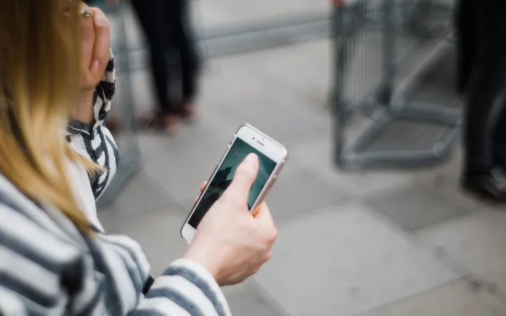 Person holding a smartphone with a photo of a pyramid, standing near a shopping cart in an outdoor area with a tiled pavement.