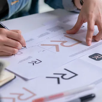 Two people review and mark a printed document with graphs and charts, with one person writing and the other pointing at the paper.