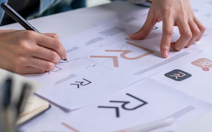 Hands working on a branding or logo design project with sketches, graphs, and branding elements on paper.