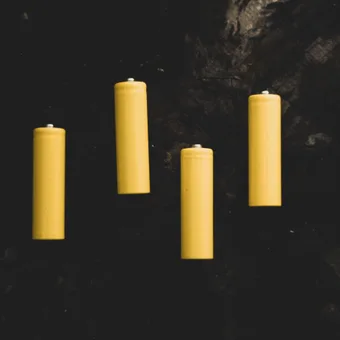 Four yellow candles are placed on a dark, rocky surface.