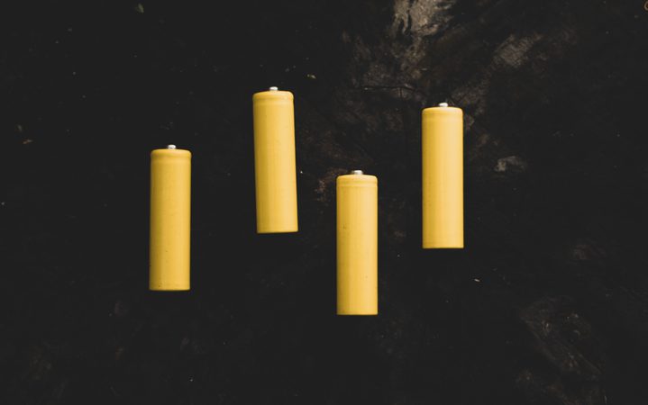 Four yellow candles are placed on a dark, rocky surface.