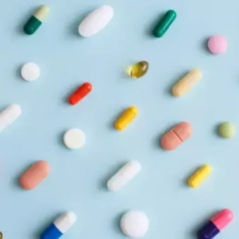 Various colourful pills and tablets scattered on a light blue background.