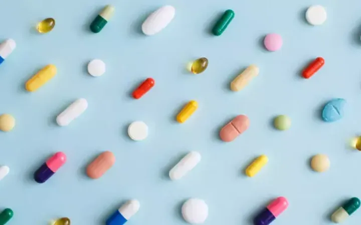 Various colourful pills and tablets scattered on a light blue background.