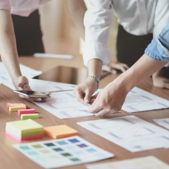 People collaborating on a project around a table with papers, sticky notes, a laptop, and supplies.