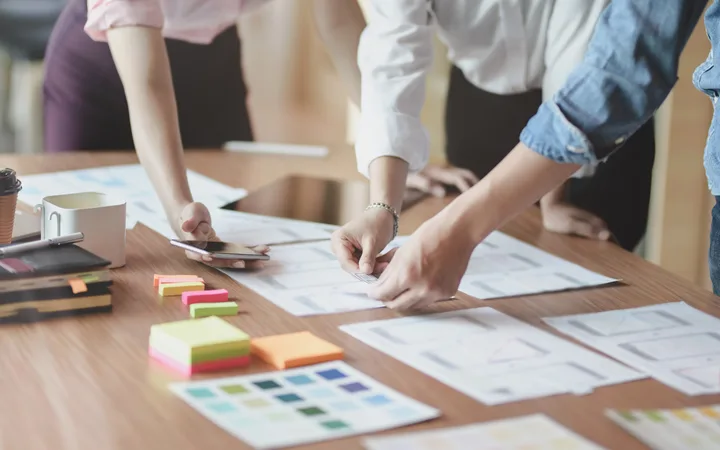 People collaborating over design sketches and notes on a table in a bright office setting.