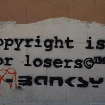 Graffiti on a wall reads "Copyright is for losers" with some graffiti tags, black stencil font on a brick wall background.