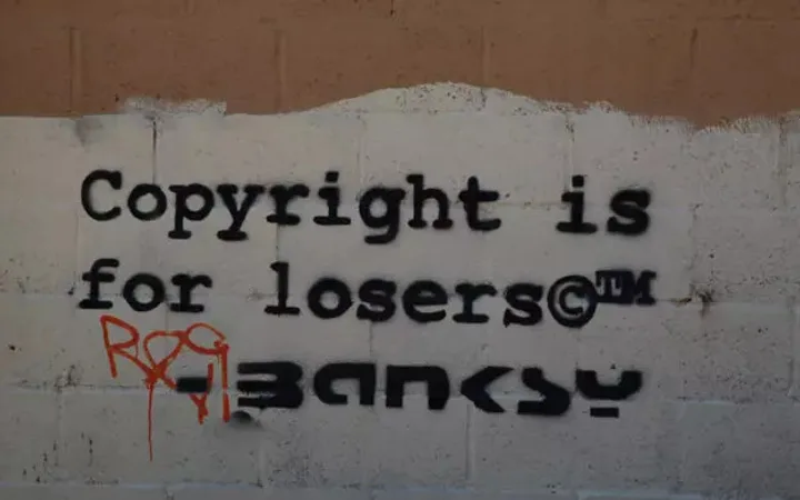 Graffiti on a wall reads "Copyright is for losers" with some graffiti tags, black stencil font on a brick wall background.