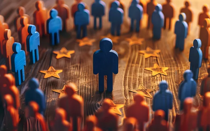 A group of blue and orange wooden human-shaped figures arranged in a circle on a wooden surface, with one figure in the centre surrounded by star-shaped decorations.