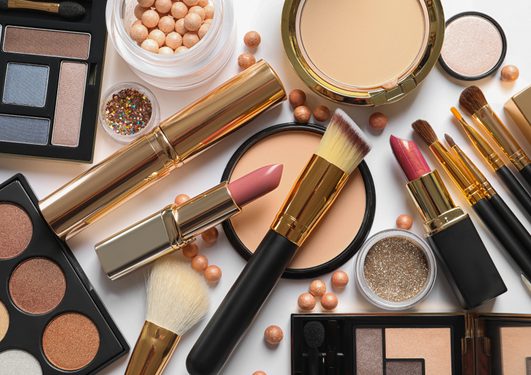 An assortment of makeup items including eyeshadow palettes, powders, lipsticks, brushes and glitter, spread on a white background.