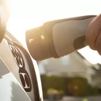 Hand using a hairdryer on a white car's dashboard with sunlight in the background.