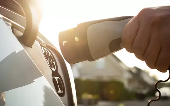Hand using a hairdryer on a white car's dashboard with sunlight in the background.