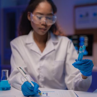 Smiling person in a gray pinstripe blazer and pale pink shirt, facing slightly left, against a neutral gray studio backdrop.